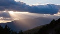 Sun shining through thick clouds over mountains right before sunset.