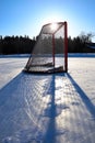 Sun silhouetting a empty hockey net on a frozen pond