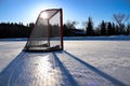 Sun silhouetting a empty hockey net on a frozen pond