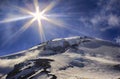 Sun and sunbeams high in the sky over the big icy mountain peak.