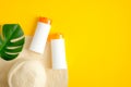 Sun tan cream and lotion bottles mockup without labels, tropical leaf and beach hat on yellow background. Top view, flat lay. Sun