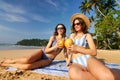 women in striped swimsuits enjoy coconut drinks on sandy beach. Sunbathers relax under tropical sun, clear blue sky Royalty Free Stock Photo