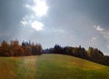 Sunbeam over a green meadow and fir trees in autumn panorama