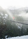 A sunbeam shines on a man with a red umbrella crossing a swinging bridge in Canada Royalty Free Stock Photo