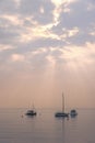 Sunbeams burst through clouds over Lake Garda, casting a spotlight on sailboats and birds in the misty pastel light Royalty Free Stock Photo