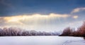 Sunbeams penetrate a dark cloud over a snow-covered field and trees. Winter landscape at sunset_ Royalty Free Stock Photo