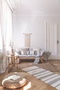 Sunbeams on a wicker ottoman and herringbone floor of a beige living room interior with a wooden sofa and cushions