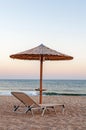 Sunbed, straw umbrella on beautiful sunset beach background