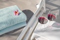 Sunbed with two towels neatly folded and a white table near it with two tall glasses of red wine, poolside inviting setting Royalty Free Stock Photo