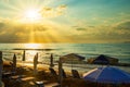 Sunbeds and straw umbrellas on sunset European beach. Crete shore, sun`s rays cut through the clouds