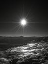 Sunburst over rocky landscape in black and white with distant mountains and bright light shining down Royalty Free Stock Photo