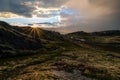 Sunburst over trail in the mountains with dramtic rain heavy clouds and blue skies to the left. Royalty Free Stock Photo