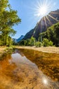 Sunburst in the sky and from the smooth Merced river looking towards half dome on the horizon in Yosemite National Park