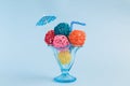 Rattan balls in form of ice cream scoops with paper parasol and drinking straw in glass cup on blue background minimalistic concep Royalty Free Stock Photo