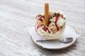 Sundae with ice cream scoops, whipped cream, red fruit sauce and chocolate sprinkles in a glass bowl on a gray table, copy space, Royalty Free Stock Photo