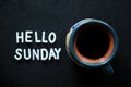 Sunday coffee. A cup of morning coffee on black table background with text sign on dark table - Hello Sunday.