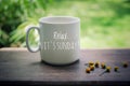 Sunday mug of coffee concept. Morning white coffee with text on it - Relax. It is Sunday, and yellow little flowers arrangement.