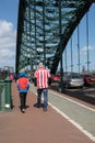 Football fans walking away from camera along pavement sidewalk on match day