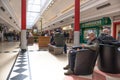 People shoppers inside a modern shopping mall sitting in a seating area. Young man using mobile phone while waiting