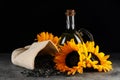 Sunflower cooking oil, seeds and beautiful flowers on grey table against black background Royalty Free Stock Photo