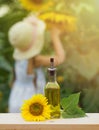Sunflower oil in a glass vessel next to a sunflower flower outdoors against the background of a little girl in a hat and Royalty Free Stock Photo