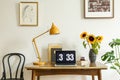 Sunflowers, yellow lamp and laptop on wooden desk in home office interior with posters. Real photo Royalty Free Stock Photo