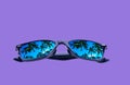 Sunglasses in a black frame with palm trees in the reflection of the lenses on a violet background, isolated Royalty Free Stock Photo