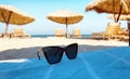 Sunglasses on blue blanket on beach white san straw awnings and armchairs on horizon green sea wave and blue sky two tent travel t Royalty Free Stock Photo