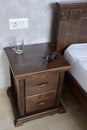 Sunglasses and an empty glass lie on a decorative brown wooden nightstand near the bed