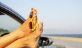 Sunglasses on female legs in a car window on the background of the sea coast. Vacation. Royalty Free Stock Photo