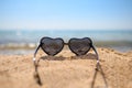 Sunglasses with glasses in the shape of a heart on a sandy beach against the background of glare of the sea and sky.