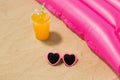 Sunglasses, juice and pool mattress on beach sand