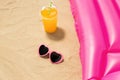 Sunglasses, juice and pool mattress on beach sand