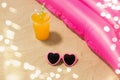 Sunglasses, juice and pool mattress on beach sand