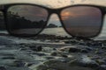 Sunglasses over the lens on the volcanic beach during the sunset