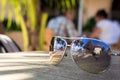 Sunglasses with a reflection of palm trees, sea and the sky lie on a table in a cafe in a tropical country