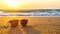 Sunglasses rest on a sandy beach with the ocean and vibrant sunset reflecting in the lenses Royalty Free Stock Photo