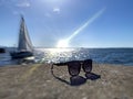 Sunglasses on rock at beach ,sea water reflection blue sky clouds sun beams and yacht boat on horizon nature landscape