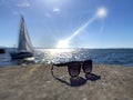 Seascape Sunglasses on rock at beach ,sea water reflection blue sky clouds sun beams and yacht boat on horizon nature landscape