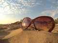 Sunglasses in the sand on shore. Concept: relax, tourism, beach vacation, travel. Reflection of the setting sun