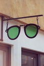 Sunglasses signboard on building. Green eyewear shaped sign on a shop wall. Store showcase fragment close up