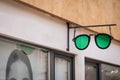Sunglasses signboard on building. Green eyewear shaped sign on a shop wall. Store showcase fragment close up