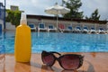 sunglasses and sunscreen around the pool against a background of blue water. Dark tinted sunglasses with drops of water Royalty Free Stock Photo