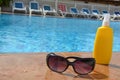 sunglasses and sunscreen around the pool against a background of blue water. Dark tinted sunglasses with drops of water Royalty Free Stock Photo