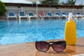 sunglasses and sunscreen around the pool against a background of blue water. Dark tinted sunglasses with drops of water Royalty Free Stock Photo