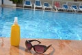 sunglasses and sunscreen around the pool against a background of blue water. Dark tinted sunglasses with drops of water Royalty Free Stock Photo
