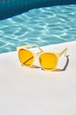 Sunglasses on a table near a pool with a blue background and yel