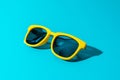 Close-up image of plastic sunglasses on turquoise blue background in perspective. Minimalist photo of stylish yellow sunglasses