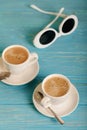 Sunglasses and two white cups of coffee on a wooden blue background. Royalty Free Stock Photo