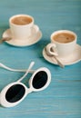 Sunglasses and two white cups of coffee on a wooden blue background. Royalty Free Stock Photo